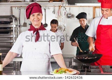 Portrait of confident female chef with colleagues cooking in commercial kitchen