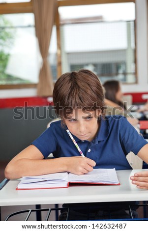 Schoolboy cheating at desk during examination in classroom