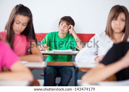 Thoughtful teenage male student looking up while sitting at desk in classroom