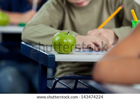 Midsection of schoolboy writing in book with apple at desk