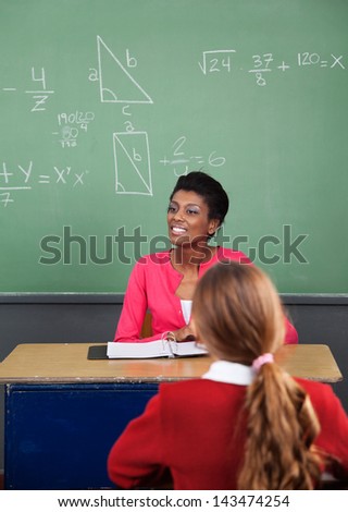 Young African American female teacher looking away with female student in foreground at classroom