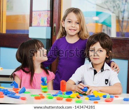 Portrait of little girl with friends playing blocks in classroom