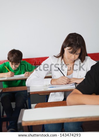Teenage schoolgirl writing paper at desk during examination in classroom