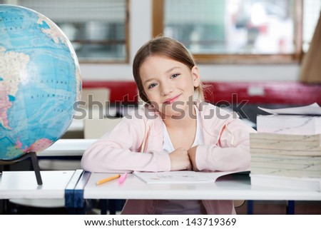 Portrait of cute little schoolgirl smiling with globe and books at desk in classroom