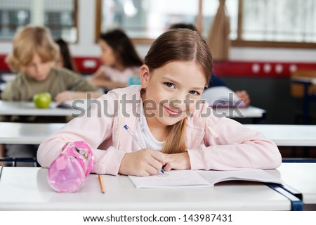 Portrait of cute little schoolgirl drawing in book with classmates in background