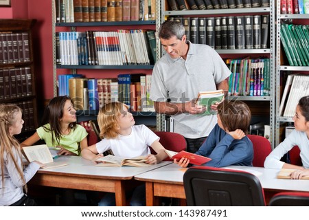 Mature male teacher communicating with students sitting at table in library