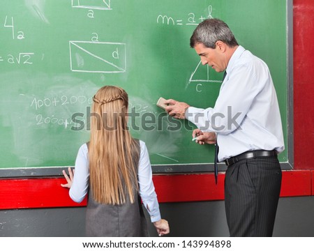 Side view of mature professor teaching mathematics to little girl on board at classroom