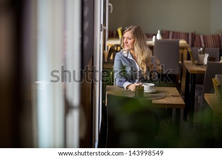 Thoughtful young woman with coffee cup sitting at table at cafe