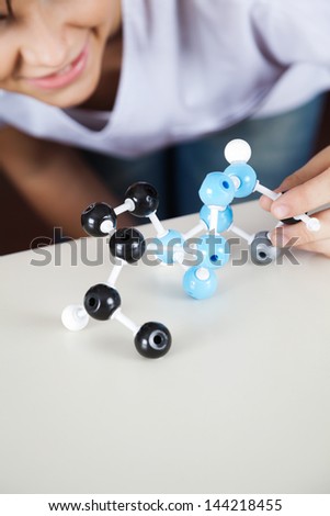 Midsection of teenage schoolgirl analyzing molecular structure at desk in classroom
