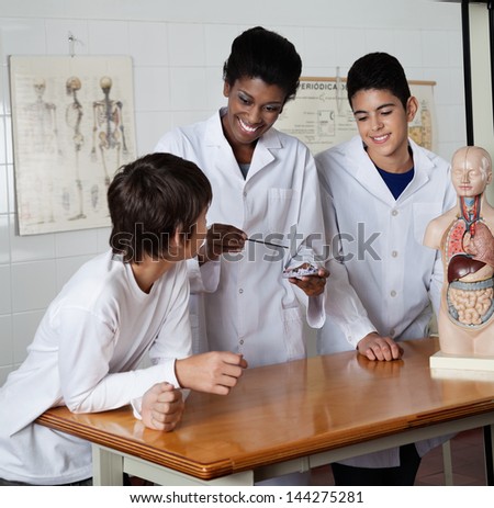 Young female teacher teaching experiment to male high school students at desk in science lab