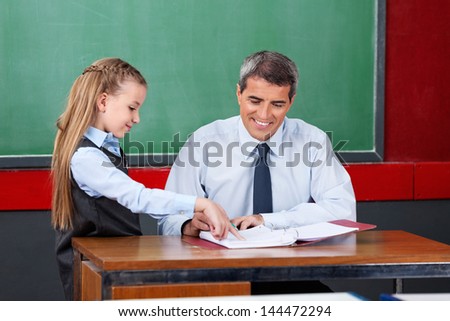 Little girl asking question to male teacher at desk in classroom