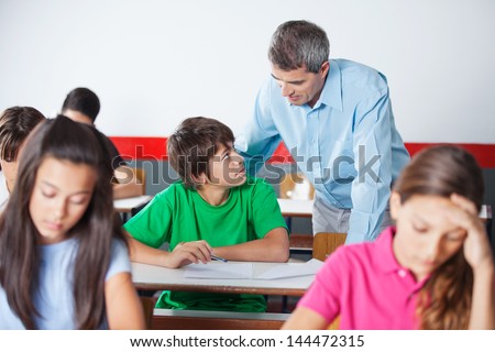 Teenage schoolboy and male teacher looking at each other during examination at desk in classroom