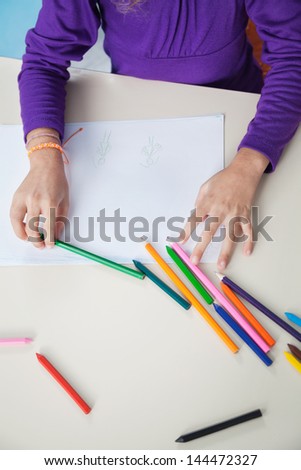Cropped image of girl with color pencils and paper at desk in classroom