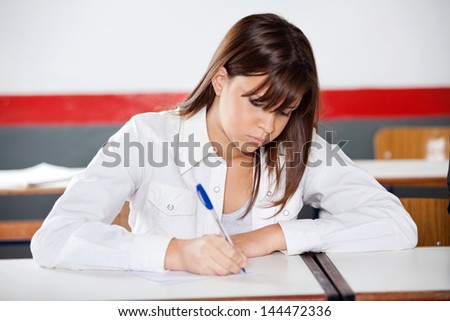 Teenage schoolgirl writing on paper during examination at desk in classroom