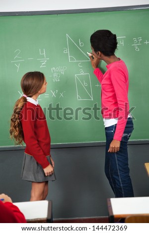 Side view of young female teacher teaching mathematics to teenage schoolgirl in classroom