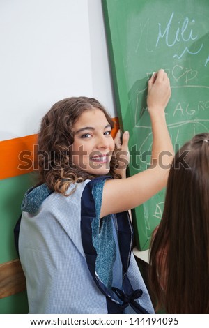 Portrait of beautiful teacher writing on chalkboard in classroom
