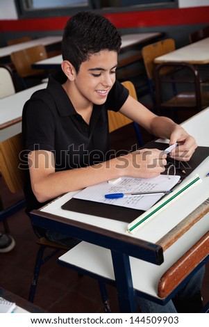 Teenage schoolboy copying from cheat sheet at desk during examination in classroom