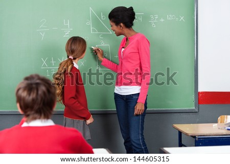 Young female teacher teaching mathematics to students on board in classroom