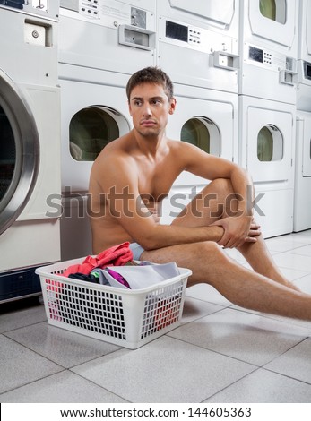 Bored young man with laundry basket waiting to wash clothes in laundry