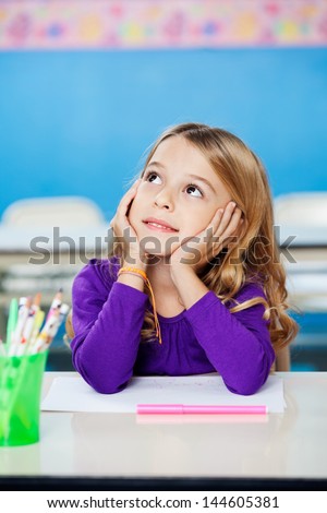 Pretty little girl looking up while sitting with head in hands in drawing class