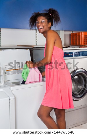 Portrait of happy young African American woman putting clothes in washing machine at laundry