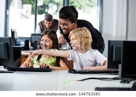 Female teacher assisting boy pointing on computer in lab at school