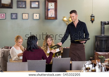 Young waiter giving menu to female customers at restaurant