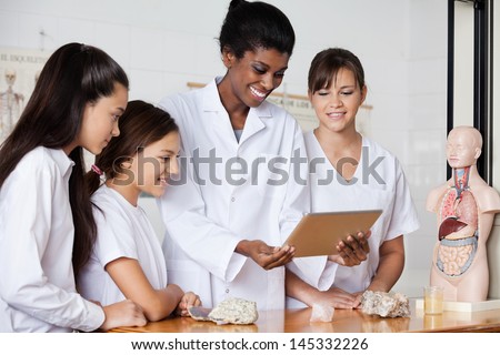 Young teacher with teenage girls using digital tablet at desk in biology class