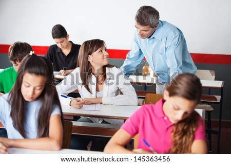Happy male teacher and teenage girl looking at each other during examination at desk in classroom