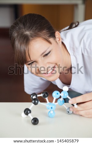 Happy high school female student looking at molecular structure at desk in classroom