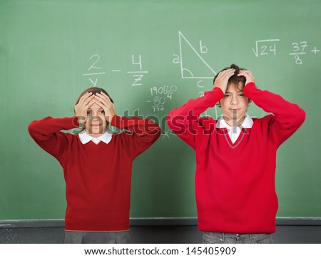 Portrait of confused teenage students standing against board in classroom