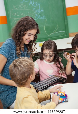 Young preschool teacher and children playing with xylophone in music class