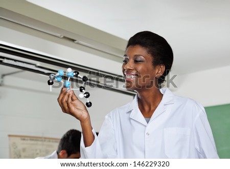 Young teacher smiling while looking at molecular structure in lab