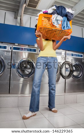 Young woman carrying basket of dirty clothes in front of her face at laundromat