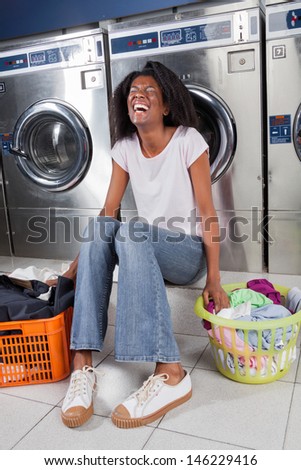 Cheerful young woman with clothes baskets sitting in laundry