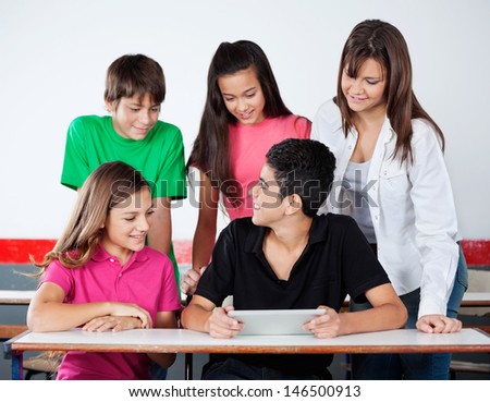 Teenage university students using digital tablet at desk in classroom