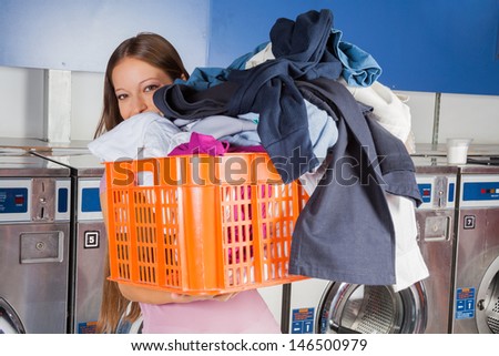 Portrait of young woman carrying basket full of dirty clothes in laundry
