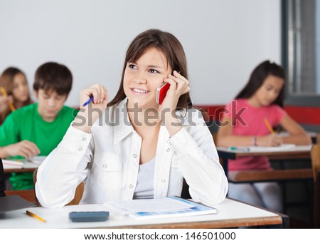 Teenage female student looking away while using mobilephone in classroom