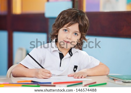 Portrait of cute boy with sketch pen and paper at desk in classroom
