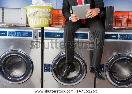 Low section of young businessman using digital tablet while sitting on washing machine