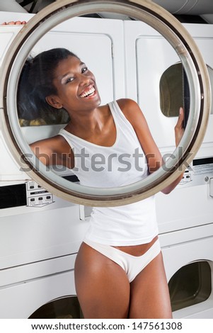 Portrait of happy young woman in undergarments looking through washing machine door