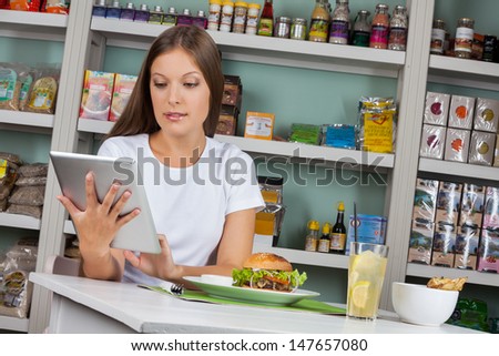 Young woman using digital tablet while having snacks in supermarket