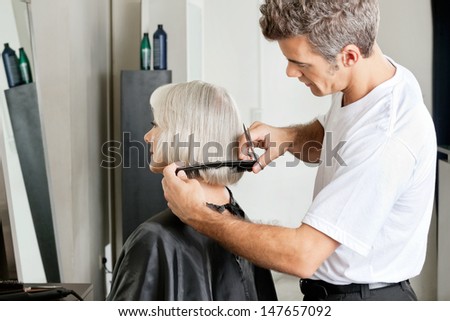 Side view of hairdresser examining hair length of female client at salon