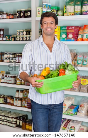 Portrait of happy mid adult man holding basket of vegetables in supermarket