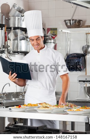 Young male chef with checklist and variety of pasta dishes at commercial kitchen counter
