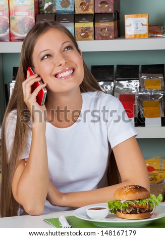 Happy young woman with snacks using cellphone at table in supermarket