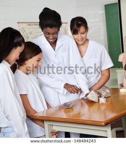 Female teacher pointing on stone while standing with female students at desk in lab