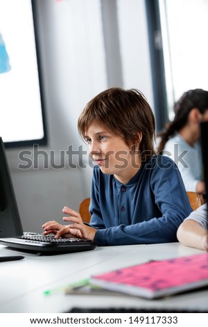 Cute little schoolboy using desktop PC at desk in computer lab