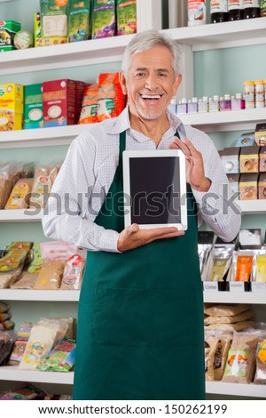 Portrait Of Happy Senior Male Store Owner Showing Digital Tablet In Supermarket