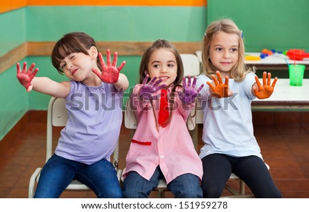 Portrait of playful little girl with friends showing colored palms in art class